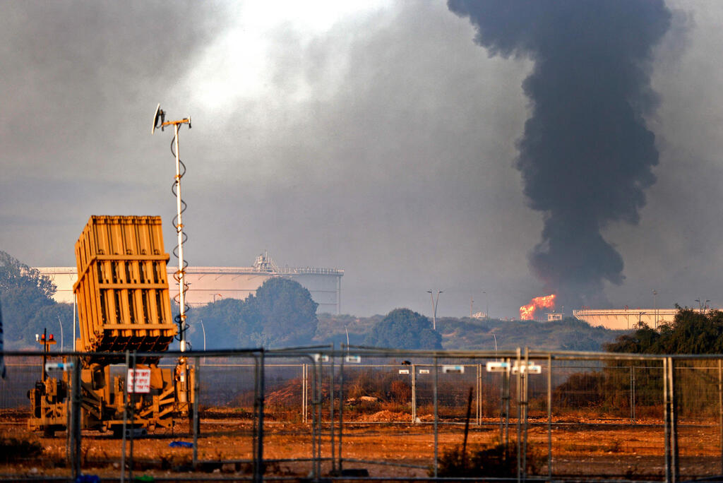 An Iron Dome missile defense battery is seen in the foreground as fire rages at Ashkelon's refinery following a rocket strike from Gaza, May 12, 2021 