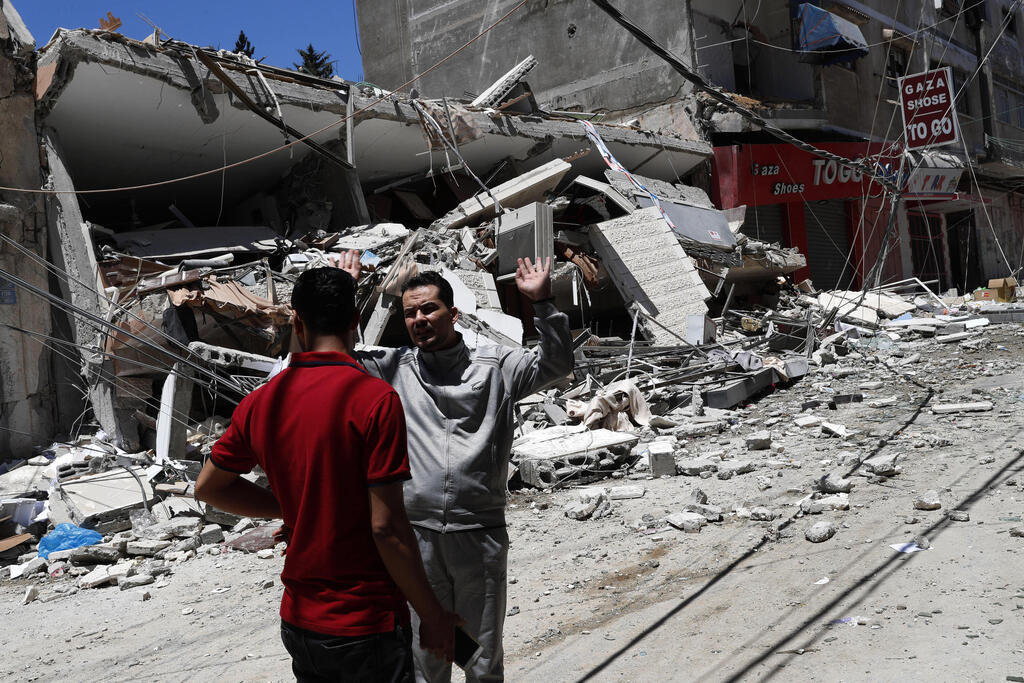 Palestinians react in front of the remains of destroyed building after being hit by Israeli airstrikes in Gaza