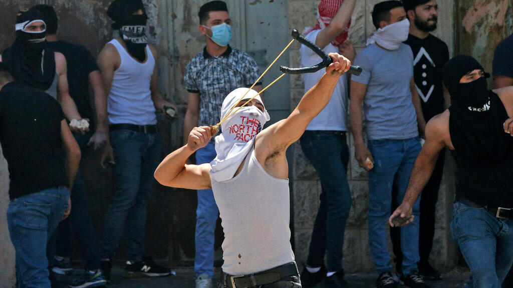 Palestinian rioter uses slingshot to hurl stones at troops in Hebron on Friday 