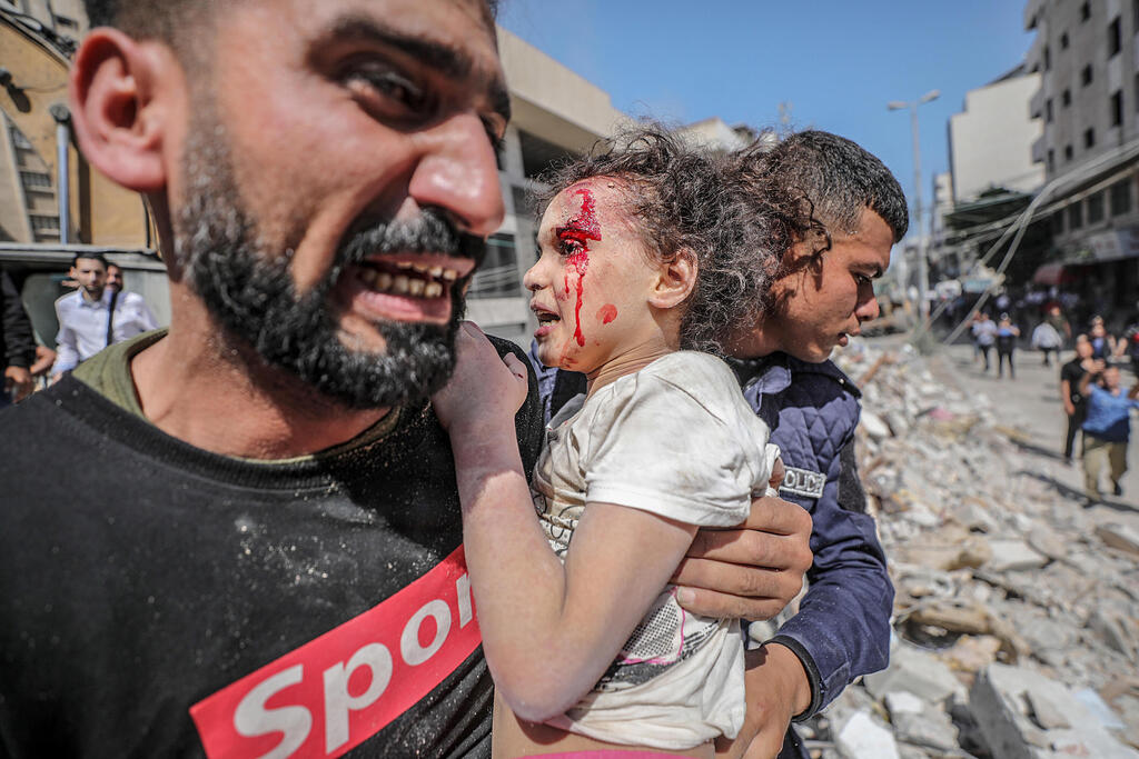 A Palestinian man holds a wounded child following an IDF strike on Gaza on Sunday   