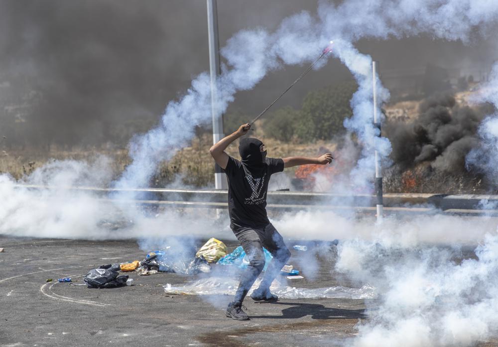 a Palestinian demonstrator uses a slingshot to return a teargas canister toward soldiers during clashes with Israeli troops at the northern entrance of the West Bank city of Ramallah 