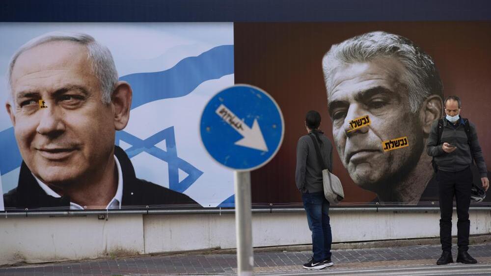 people stand in front of an election campaign billboard for the Likud party showing a portrait of its leader Prime Minister Benjamin Netanyahu, left, and opposition party leader Yair Lapid, in Ramat Gan, Israel 