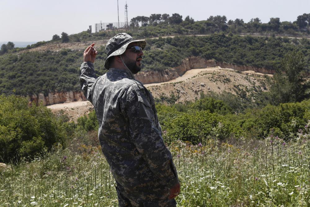 a Hezbollah officer, who identified himself as Ehab, stands in front an Israeli army position, background, as he explains to journalists about the defensive measures established by the Israeli forces, how they cut through the mountain to prevent against any Hezbollah infiltration into Israel, at the Lebanese-Israeli border near the village of Labbouneh, south Lebanon 