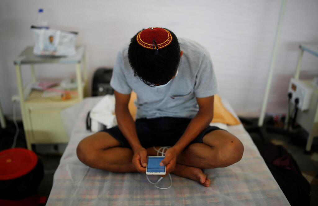 An Indian Jew, member of the Bnei Menashe, or the Children of Menashe, one of the "lost tribes of Israel" from the India's northeastern state of Manipur, suffering from the coronavirus disease (COVID-19), checks his mobile phone as he sits on a bed at a COVID-19 care facility, inside a Gurudwara or a Sikh Temple, in New Delhi, India 