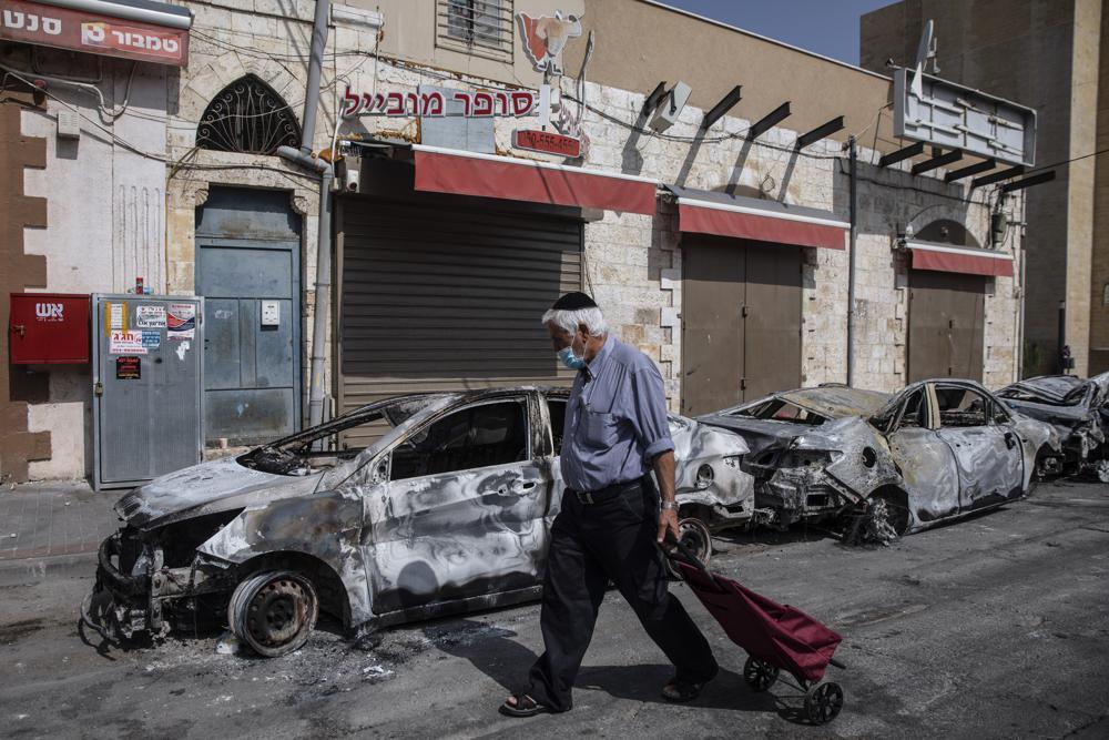 A man passes by cars torched after a night of violence between Israeli Arab protesters and Israeli police in the mixed Arab-Jewish town of Lod, central Israel, Tuesday, May 11, 2021 