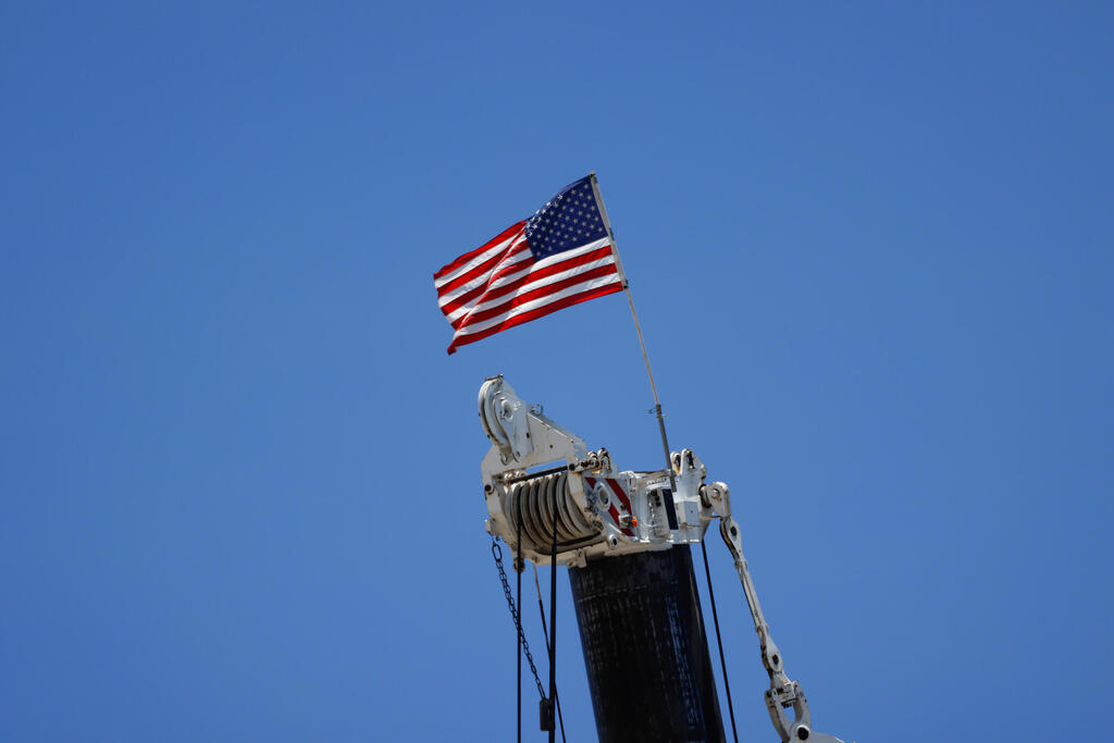 An American flag flutters atop a crane at the site of a partially collapsed residential building
