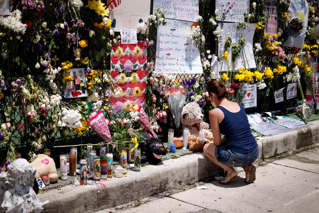 A woman kneels at a memorial site created by neighbors in front of a partially collapsed residential building on Sunday 