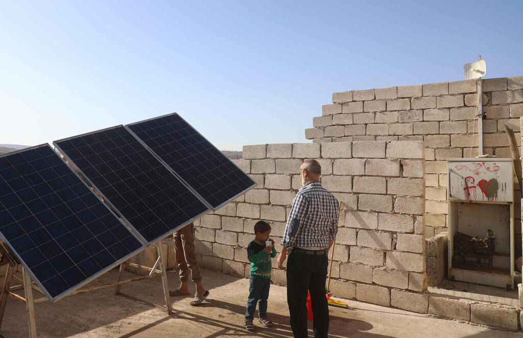 Zakariya Sinno and his son stand near a solar panel installed on the rooftop of his house in the village of Killi, near Bab al-Hawa by the border with Turkey, in Syria's northwestern Idlib province, on June 9, 2021