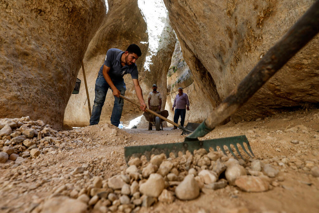 Volunteers rake stones between cliffs in the village of Maalula 