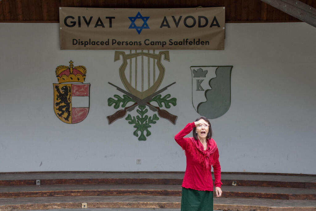 An actress of the theater group Teatro Caprile gestures during a scene as she stands in front of a banner reading "Givat Avoda", which translates to "Hill of Labour", in the Krimmler Tauern Alps 