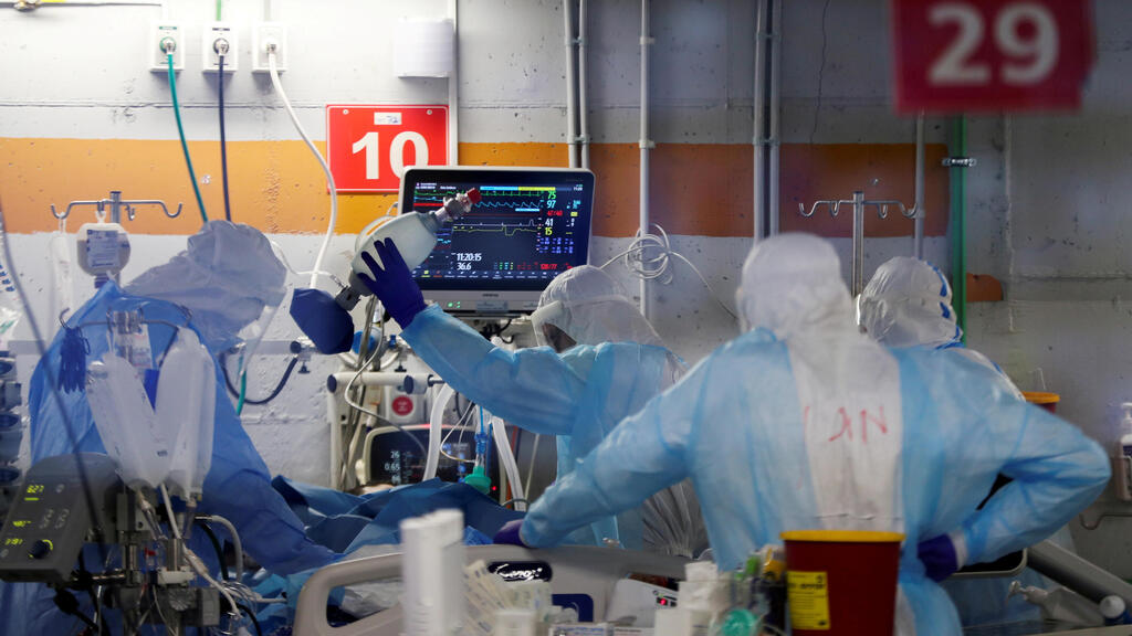 Medical workers, seen through a window of an observation room, wear personal protective equipment (PPE) as they work inside an underground ward 