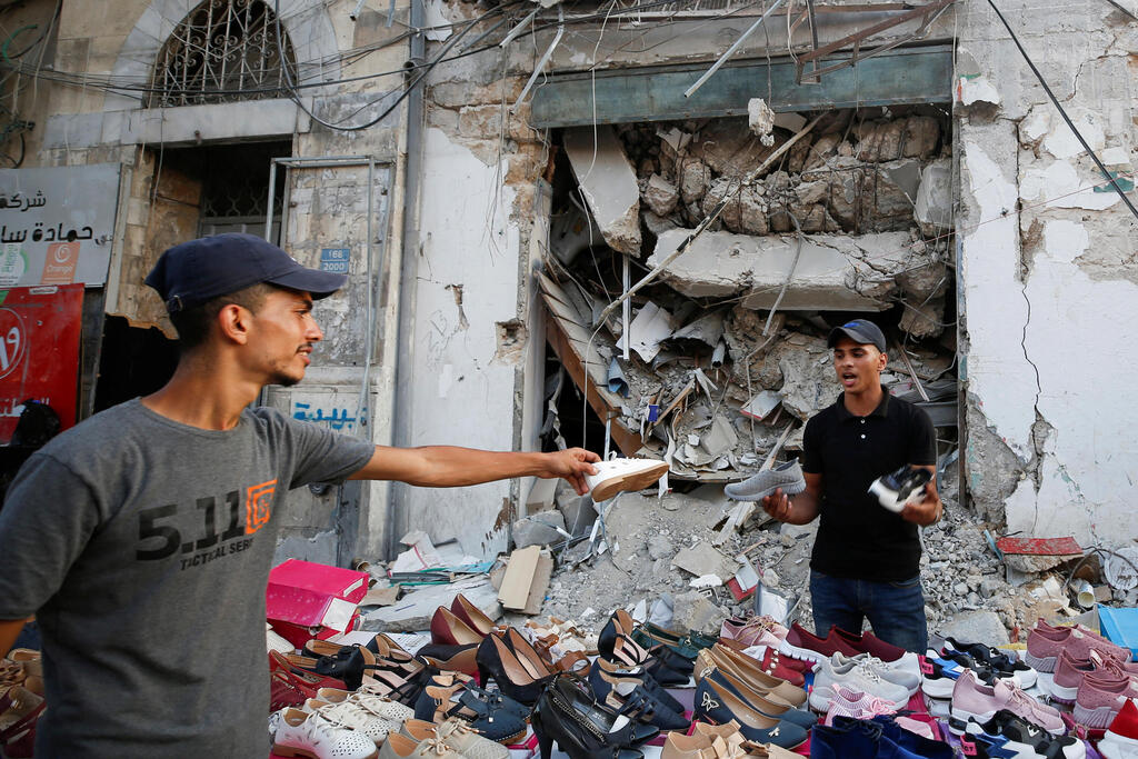A Palestinian sells shoes on a stall near the rubble of his old shoe store that has been destroyed in an Israeli air strike, ahead of Eid Al-Adha Muslim holiday, in Gaza City 