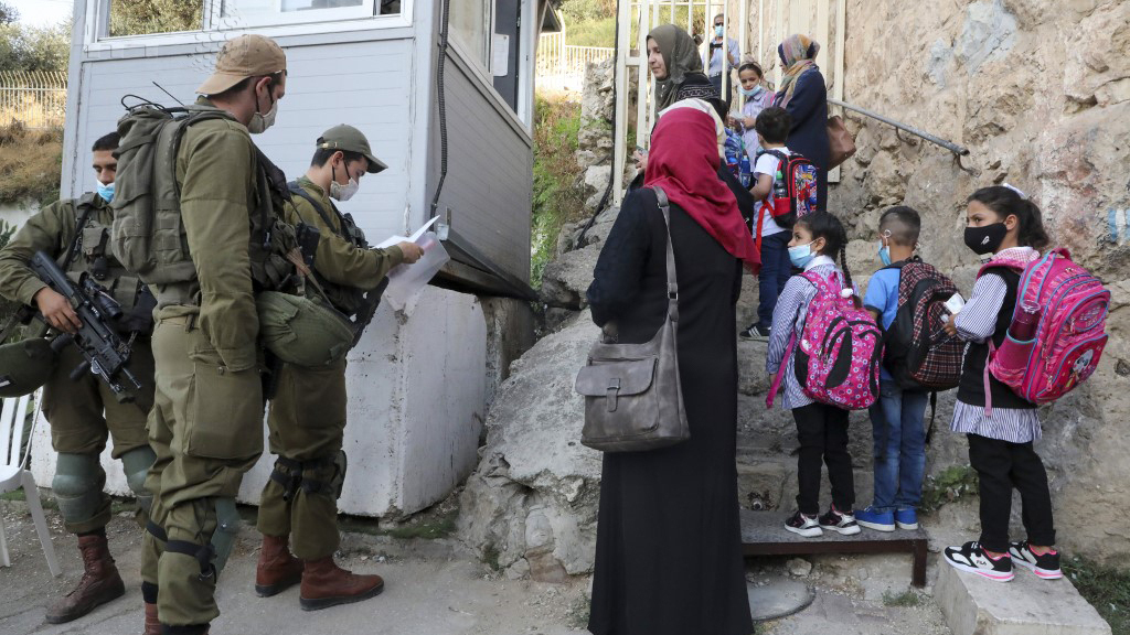 Palestinian students and teachers wait for Israeli soldiers to allow them to cross a military checkpoint near the Jewish settlement of Beit Hadasa in the occupied West Bank city of Hebron 