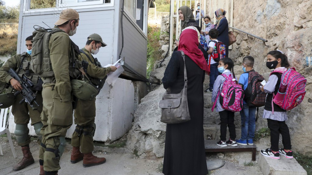 Palestinian students and teachers wait for Israeli soldiers to allow them to cross a military checkpoint near the Jewish settlement of Beit Hadasa in the occupied West Bank city of Hebron 