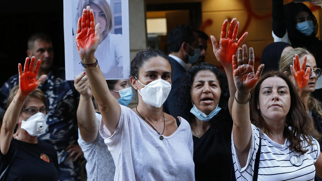 Tracy Naggear, center left, the mother of 3-year-old Alexandra, who was killed in last year's massive blast at Beirut's seaport, and relatives of others who were killed, raise their red-painted hands representing blood, during a protest outside the home of caretaker Interior Minister Mohamed Fehmi, in Beirut, Lebanon