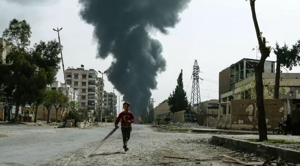 A child runs along a street in front of clouds of smoke billowing following a reported air strike on Douma, the main town of Syria's rebel enclave of Eastern Ghouta on March 20, 2018.