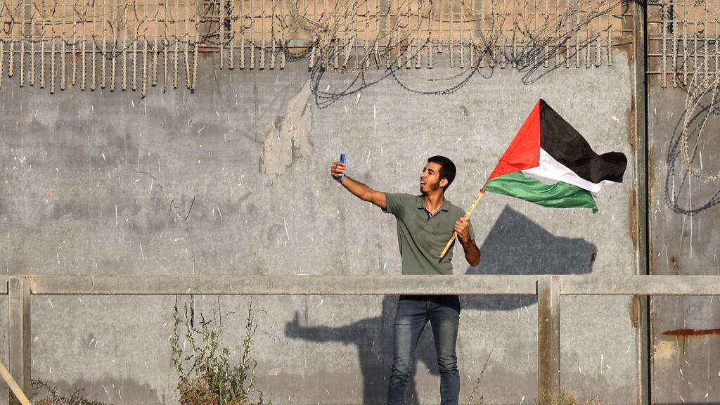 A Palestinian protester lifting a national flag takes a selfie during a demonstration by the border fence with Israel, east of Gaza City