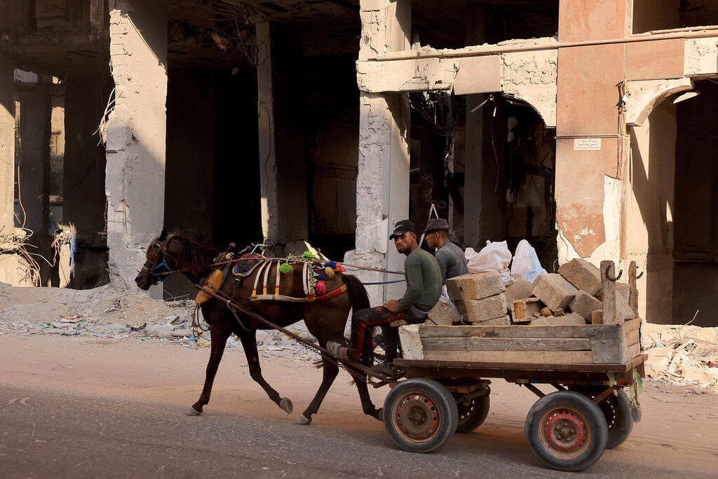 Palestinians ride a horse cart carrying rubble past the ruins of buildings destroyed in the last round of Israeli-Hamas fighting, in Gaza City, on August 25, 2021