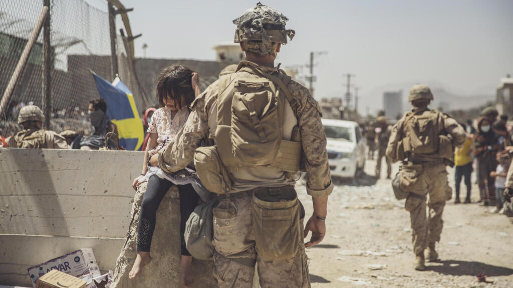 A marine cares for young child awaiting processing at an evacuation control checkpoint during an evacuation at Kabul airport 