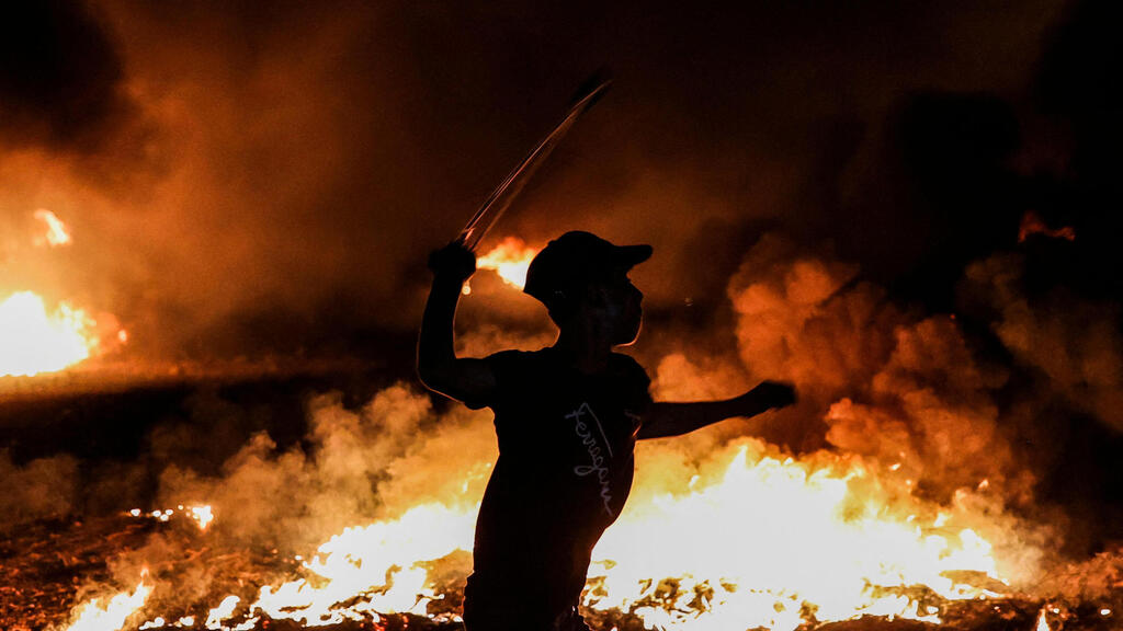 A Palestinian protester swings a slingshot near burning tyres following a demonstration along the border between the Gaza Strip and Israel east of Gaza City on August 28, 2021 