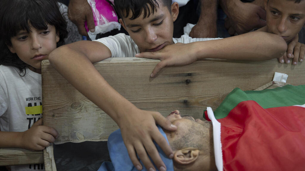 Palestinian Yousef Jadallah, places his hand on his father Raed Jadallah's body, who was killed by Israeli forces at the western entrance of his village while returning from work in the early hours of Wednesday morning