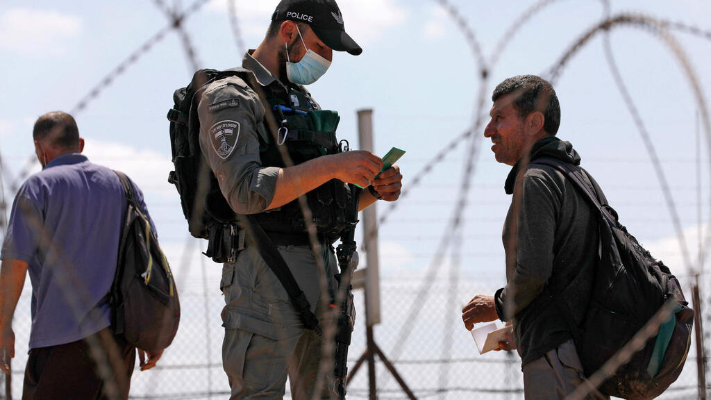Border Police officer checks documents of Palestinian crossing from Jenin (Photo: AFP) עובדים פלסטינים חוצים את הגדר סמוך לג'נין