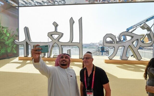 A visitor takes a selfie with Israeli pavilion official Josh Bendit in front of a sign reading ‘toward tomorrow’ in words written in characters that can be read by both Hebrew and Arabic speakers during a media preview 
