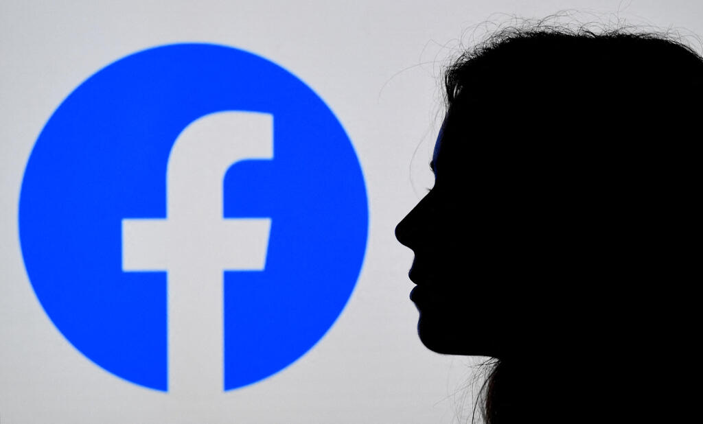 photo illustration, a person looks at a smart phone with a Facebook App logo displayed on the background