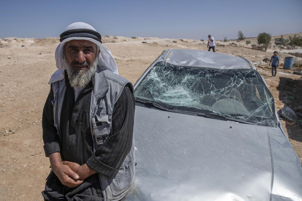 A Palestinian man leans on his smashed vehicle following a settlers attack from nearby settlement outposts on his Bedouin community, in the West Bank village of al-Mufagara