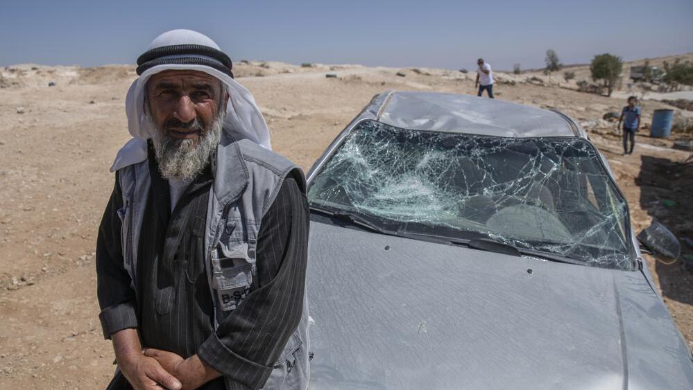 A Palestinian man leans on his smashed vehicle following a settlers attack from nearby settlement outposts on his Bedouin community, in the West Bank village of al-Mufagara