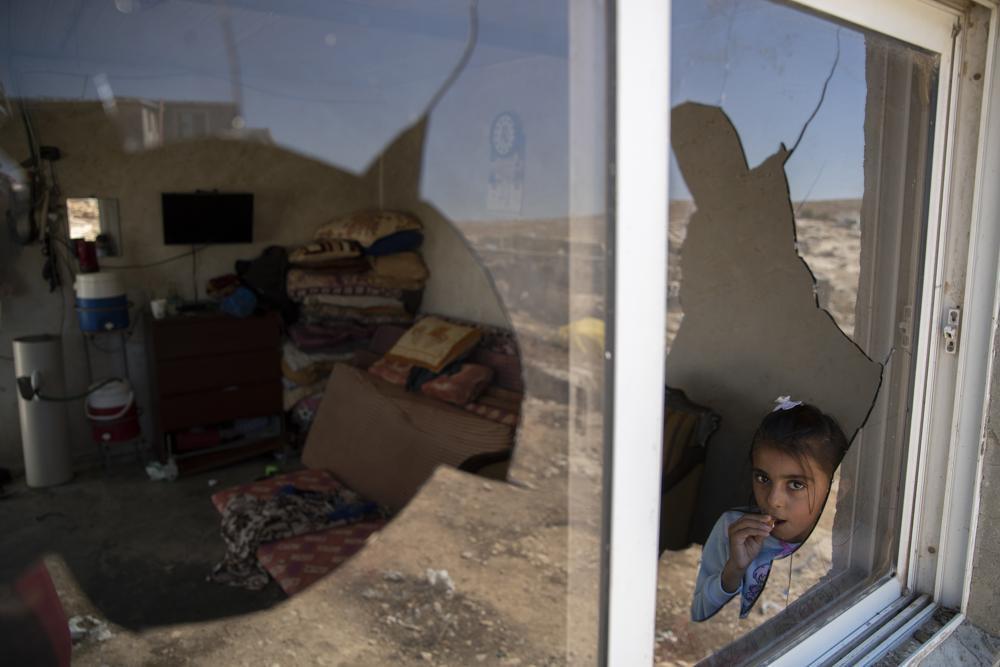 A Palestinian girl is seen through her family house's shattered window following a settlers' attack from nearby settlement outposts on the Bedouin community, in the West Bank village of al-Mufagara