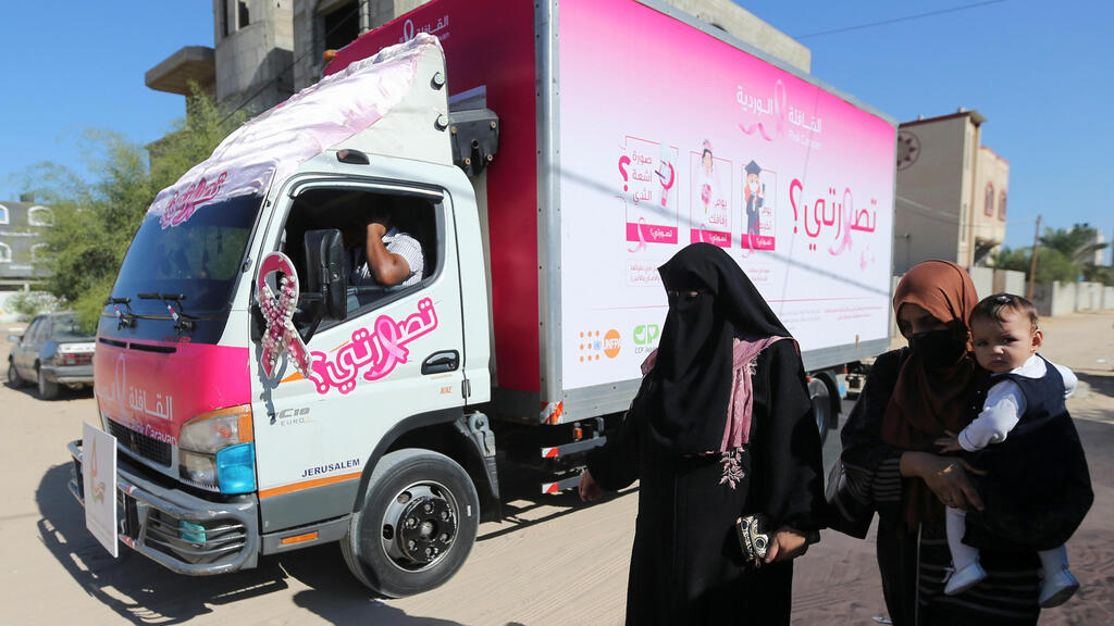 Palestinian women walk past a mobile breast cancer check up clinic set up in a truck, during a campaign aimed to raise public awareness in Gaza 