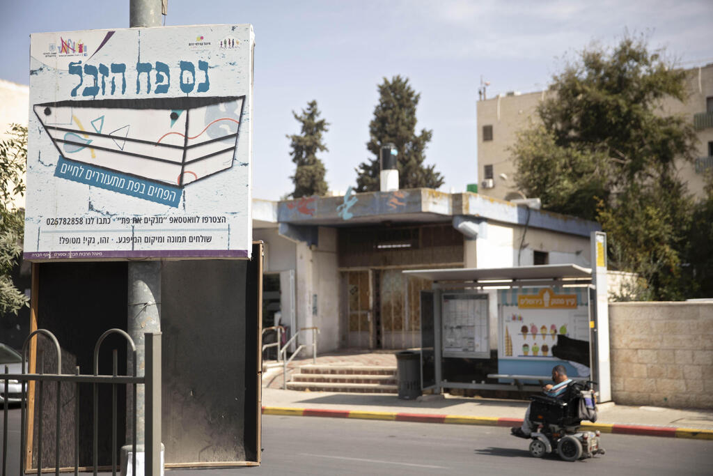 A sign that reads 'the trash can miracle' hangs across the street from a trash can installed at a bus stop that applauds those who use it, in Jerusalem, October 14, 2021