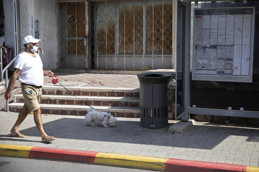 A man walks a dog near a trash can installed next to a bus stop that applauds those who use it, in Jerusalem, October 14, 2021