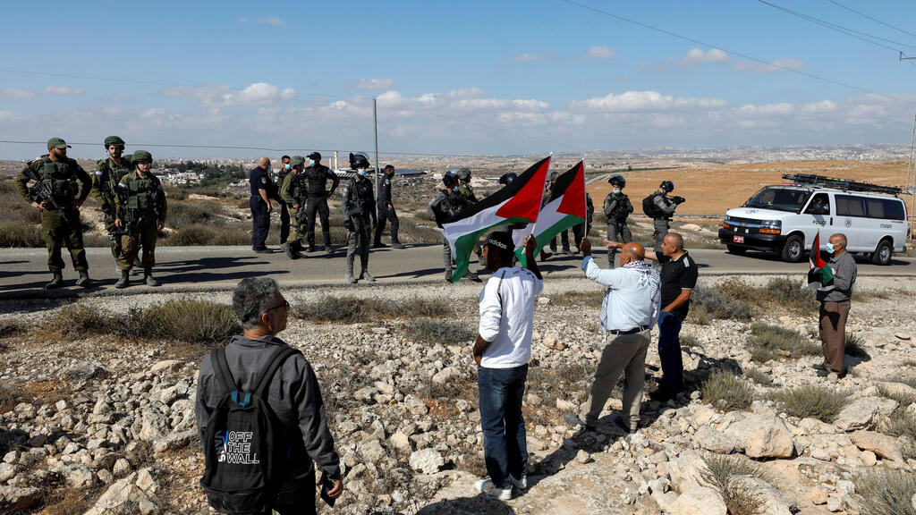 Demonstrators hold Palestinian flags as members of Israeli forces stand guard during a protest against Israeli settlements in Masafer Yatta, in the Israeli-occupied West Bank