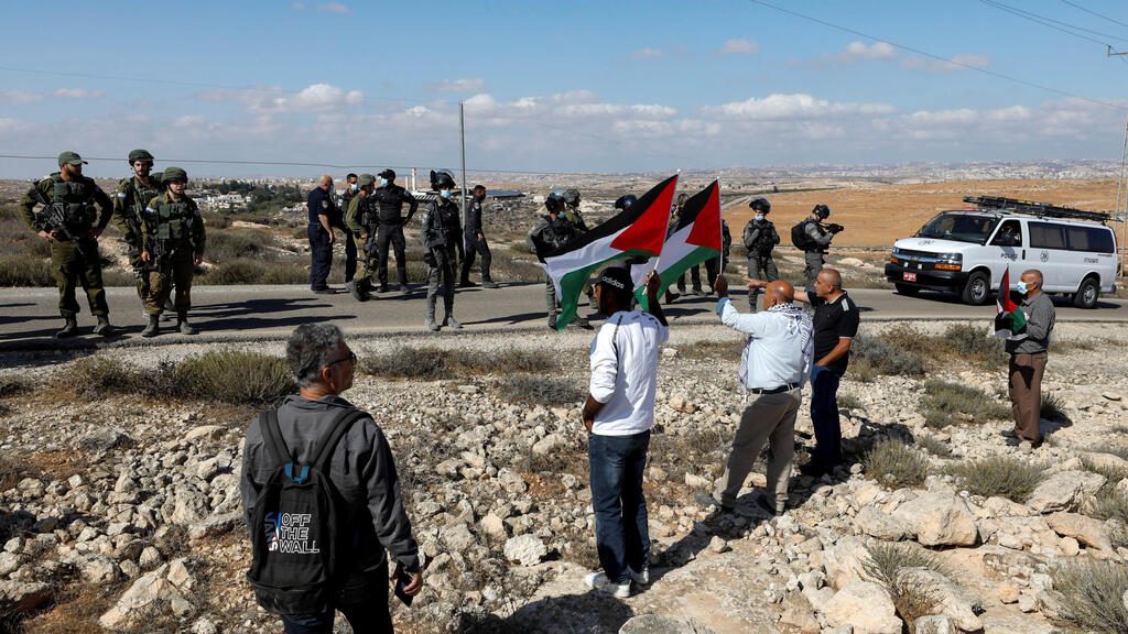 Demonstrators hold Palestinian flags as members of Israeli forces stand guard during a protest against Israeli settlements in Masafer Yatta, in the Israeli-occupied West Bank