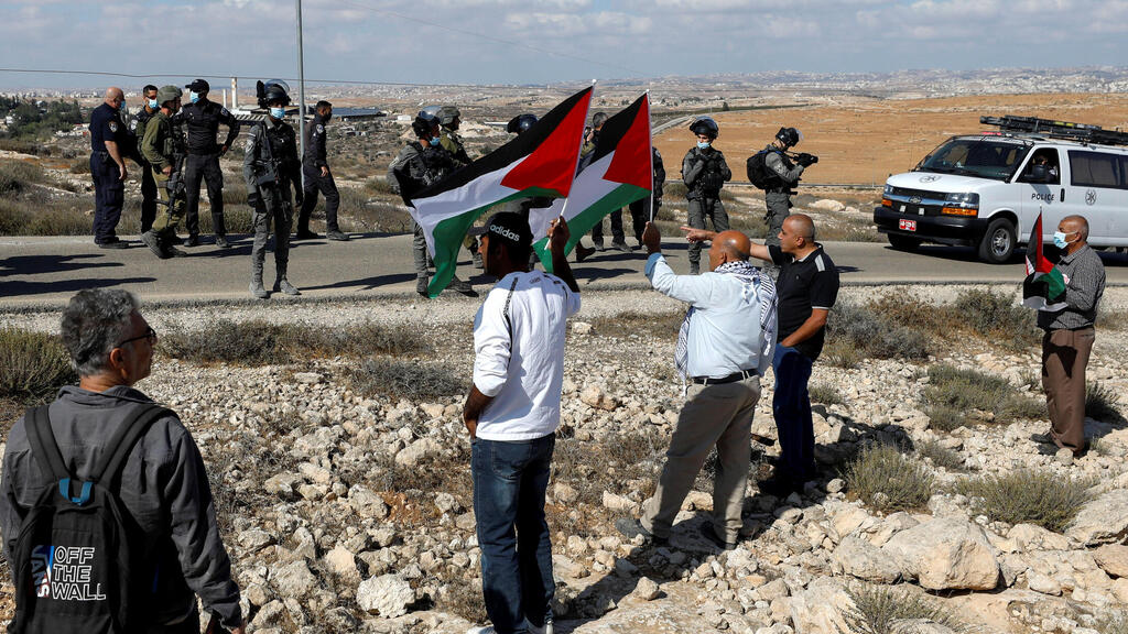 Demonstrators hold Palestinian flags as members of Israeli forces stand guard during a protest against Israeli settlements in Masafer Yatta, in the Israeli-occupied West Bank