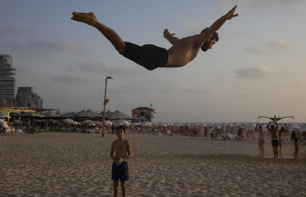 An Israeli man practices acrobatics on the beach in Tel Aviv, Israel, Saturday, Aug. 7, 2021, left, and Palestinians watch a man performs acrobatics on the beach of Gaza City, Friday, June 4, 2021, right