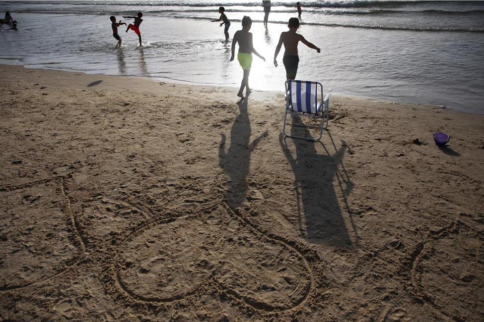 Heart shapes drawn in sand as the sun sets over Tel Aviv’s beach, Israel, Saturday, June 12, 2021, left, and a Palestinian man works on a sand shape of heart on the beach of Gaza City, Friday, July 2, 2021, right