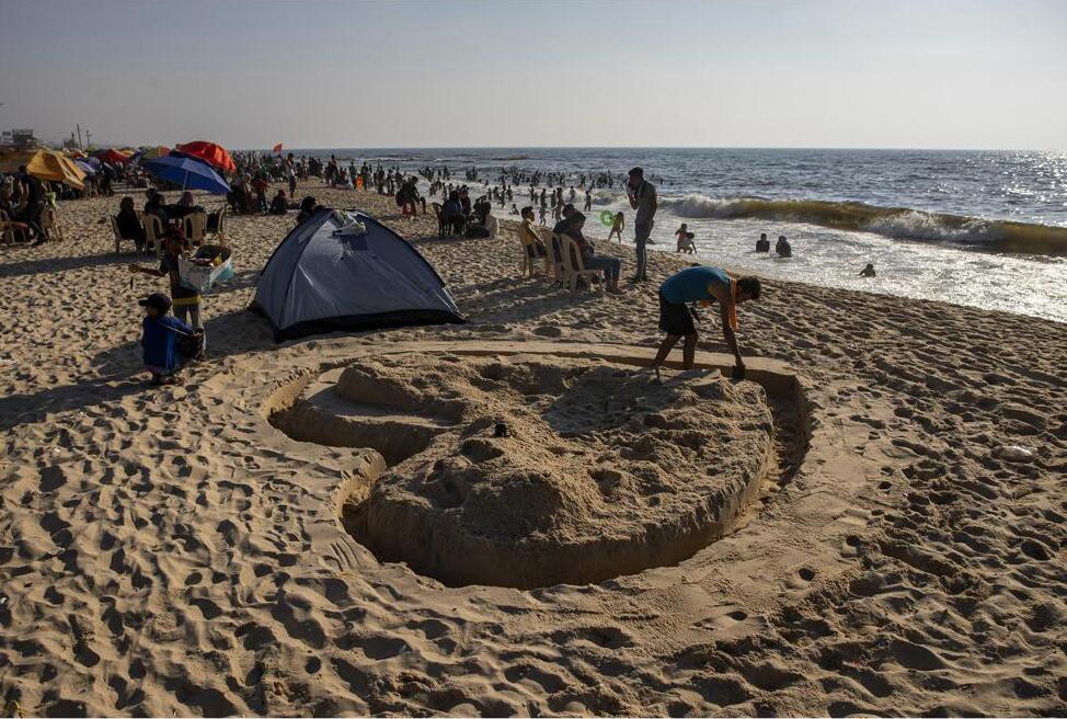 Heart shapes drawn in sand as the sun sets over Tel Aviv’s beach, Israel, Saturday, June 12, 2021, left, and a Palestinian man works on a sand shape of heart on the beach of Gaza City, Friday, July 2, 2021, right