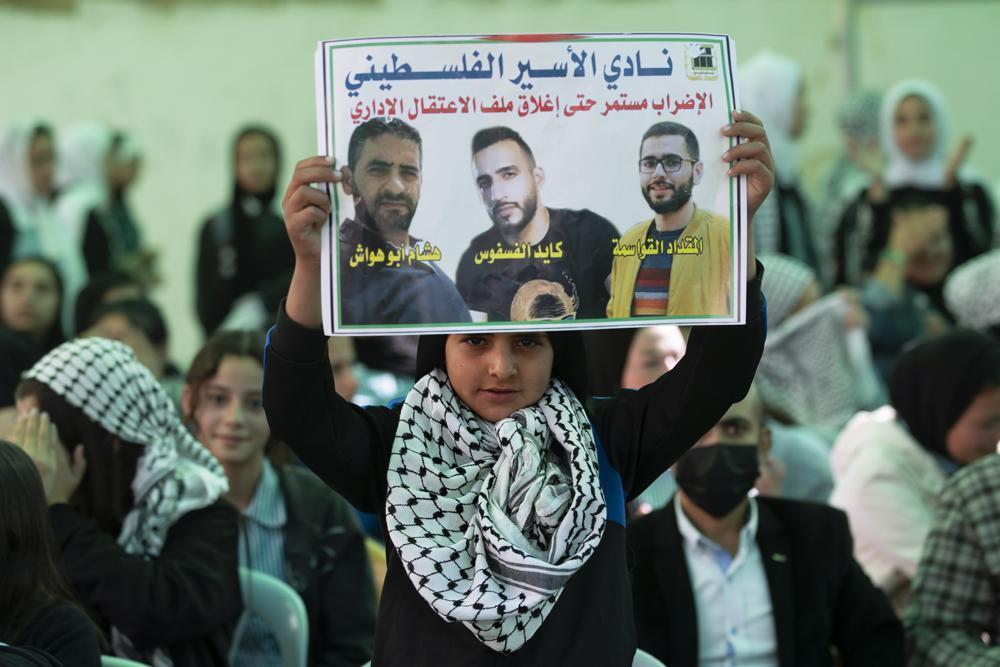 A protester holds a poster showing Kayed Fasfous, center, a Palestinian prisoner who has been on a hunger strike to protest being detained without charge by Israel, in the village of ad-Dhahiriya, near the West Bank town of Hebron 