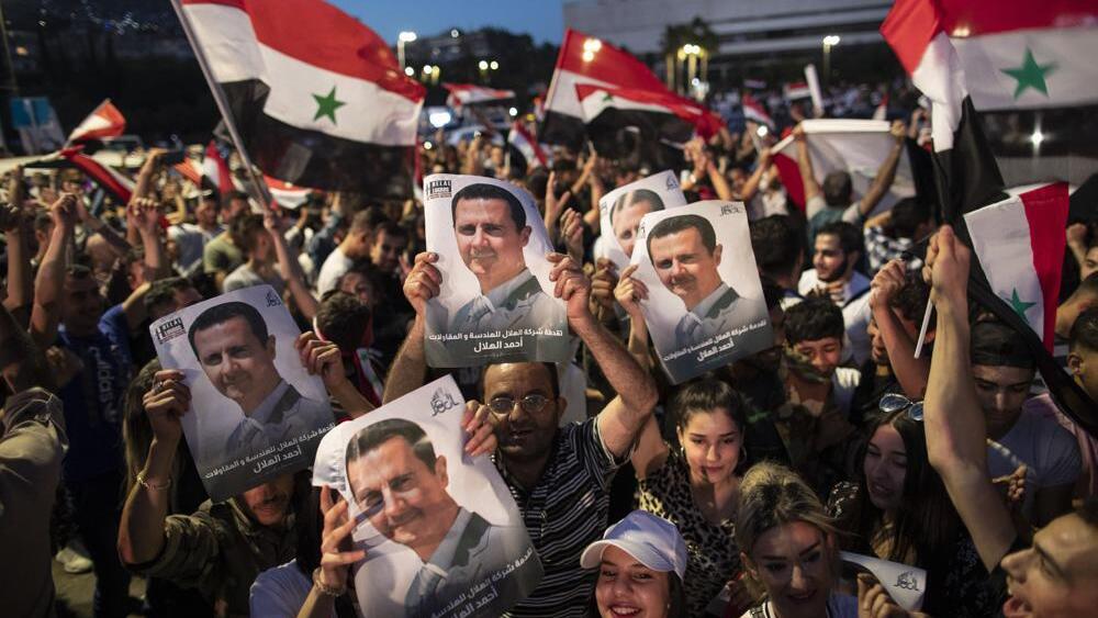 Syrian President Bashar Assad supporters hold up national flags and pictures of Assad as they celebrate at Omayyad Square, in Damascus, Syria 
