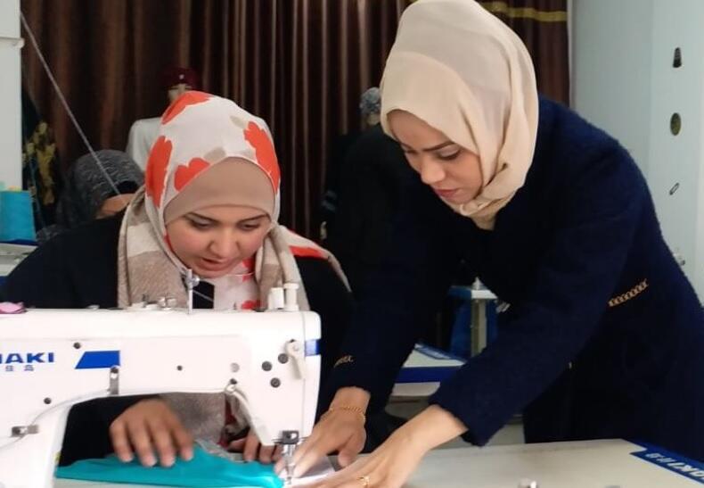 Aya Eid, right, a founder of the Khalil & Aya Fashion House in the Gaza Strip, works with a design student