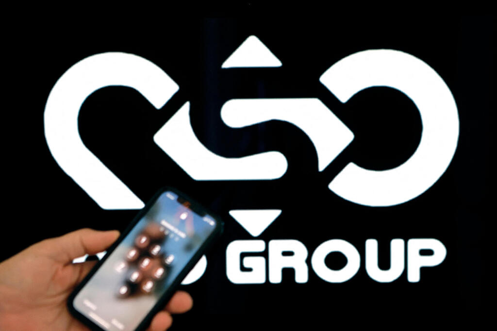 A person holding a phone in front of NSO Group logo (Photo: AFP) טלפון נייד על רקע לוגו NSO