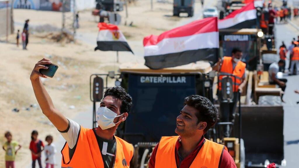 Men pose for a selfie in front of building equipment, sent by Egypt into Gaza