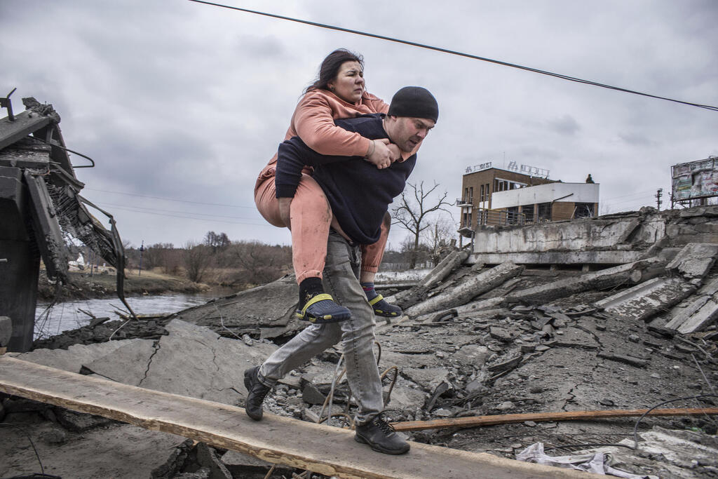 גבר נושא אישה כ שהם חוצים שביל מאולתר בזמן ש הם בורחים מ העיר אירפין, אוקראינה