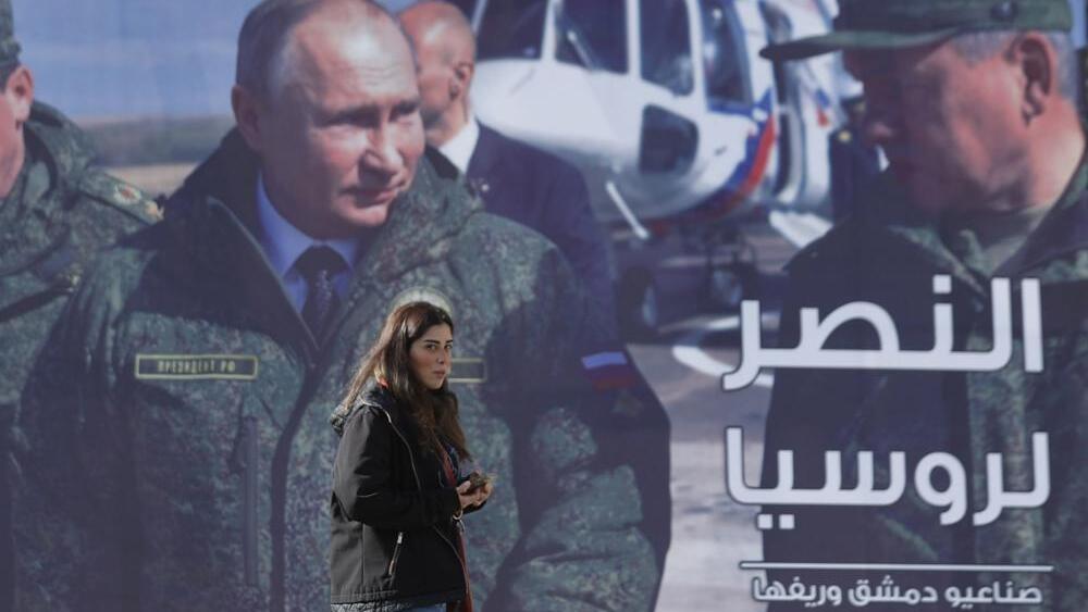 A woman passes a billboard showing Russian President Vladimir Putin in Damascus, Syria, Monday, March 7, 202