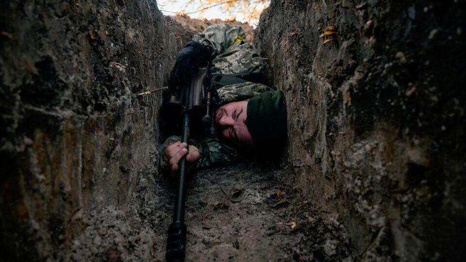 A  Ukrainian soldier hides from a helicopter airstrike amid Russia's invasion of Ukraine, near Demydiv,