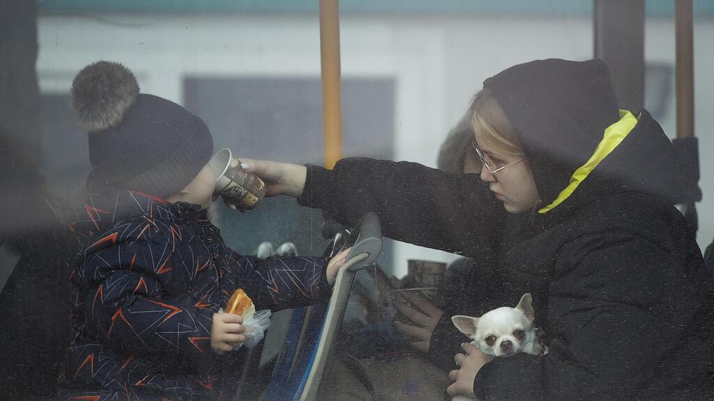  refugee holding a small dog gives a sip of tea to a toddler after fleeing the conflict from neighboring Ukraine
