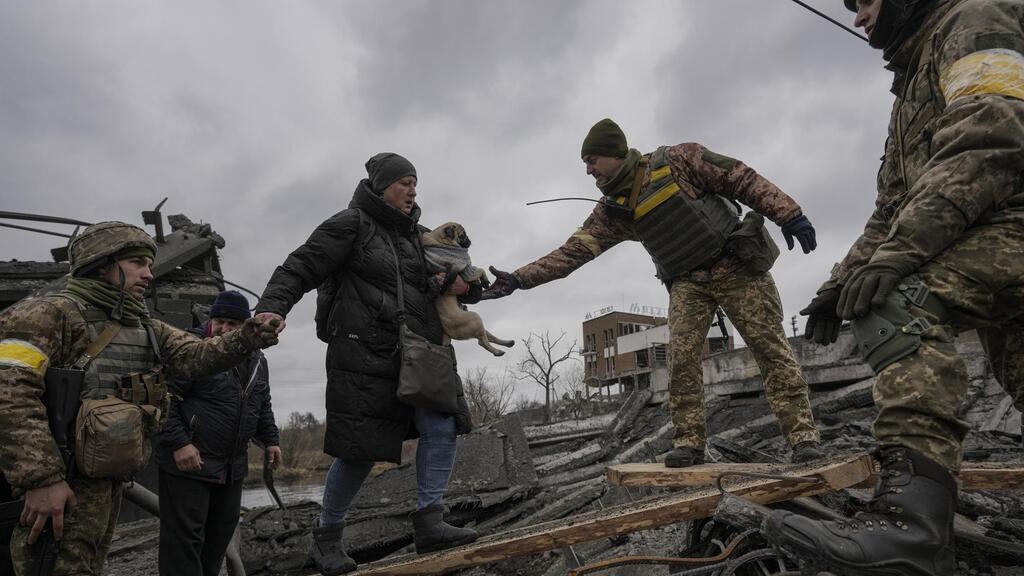 Ukrainian servicemen help a woman carrying a small dog across the Irpin River, Ukraine